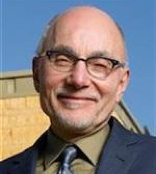 Picture of Dr. Abbeduto with suit and tie, glasses, blue sky and building background